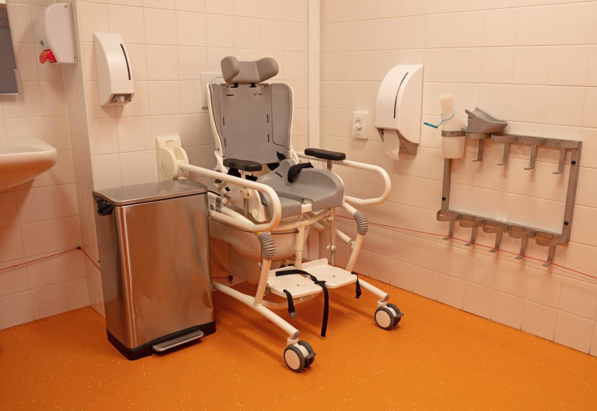 Mobile shower commode positioned over toilet in accessible bathroom