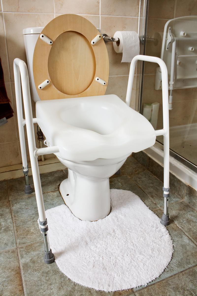 Raised toilet seat with arm rests positioned over toilet
