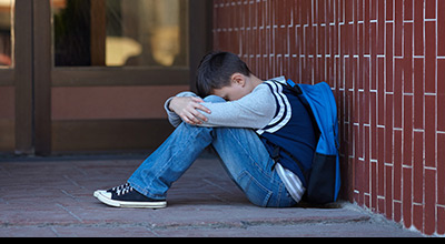 Boy with ADHD in school yard sitting with head in hands