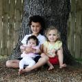 Maia and her brother and sister sitting against a tree with her brother holding her in his arms