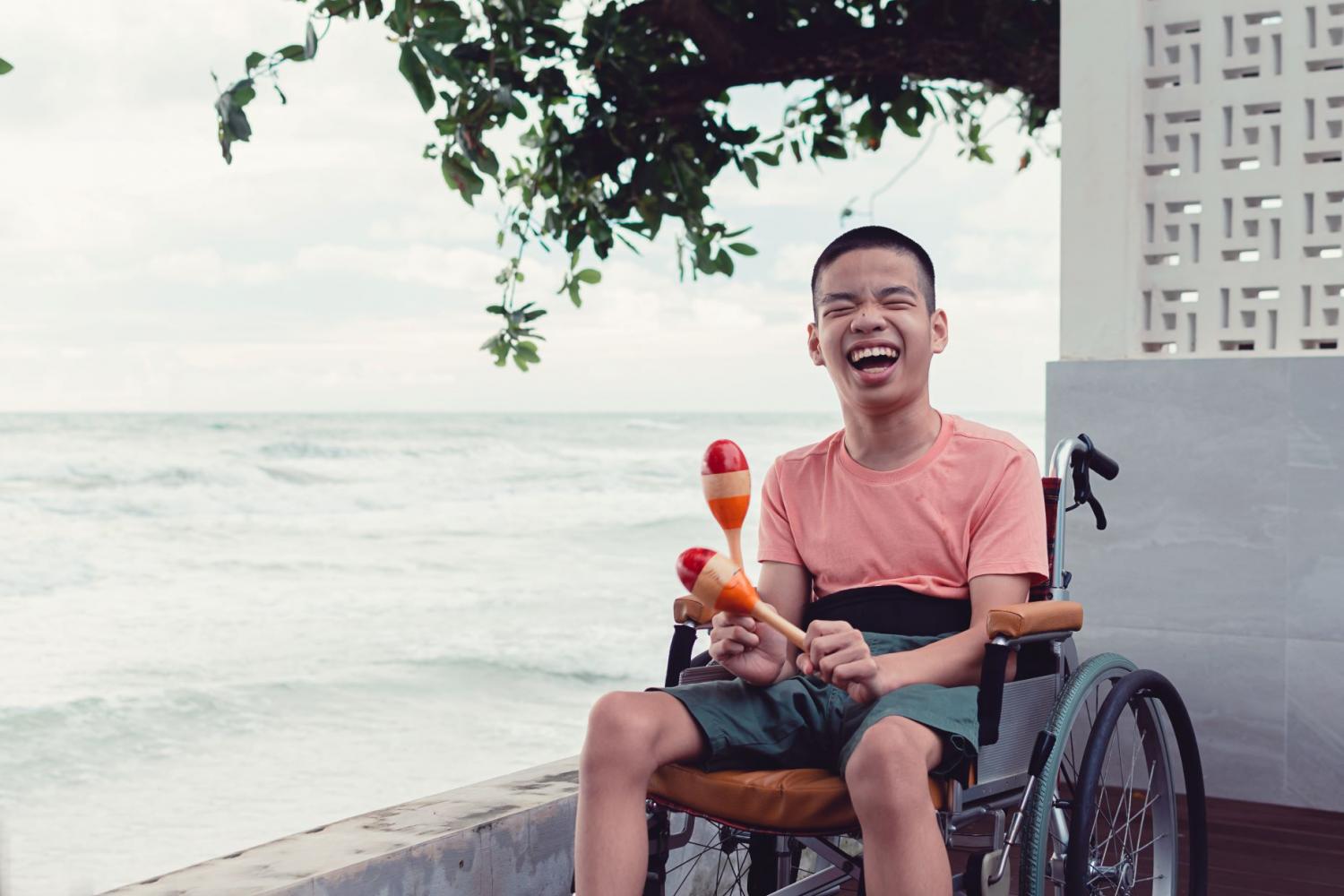 Young man seated in a wheelchair by the ocean playing with maracas