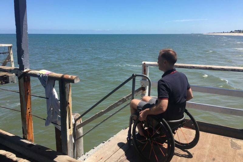 Ryan Mann sits at edge of dock in his wheelchair, looking out at the water