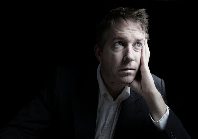 Man in a suit sits with a sad expression on his face, which is resting in his hand