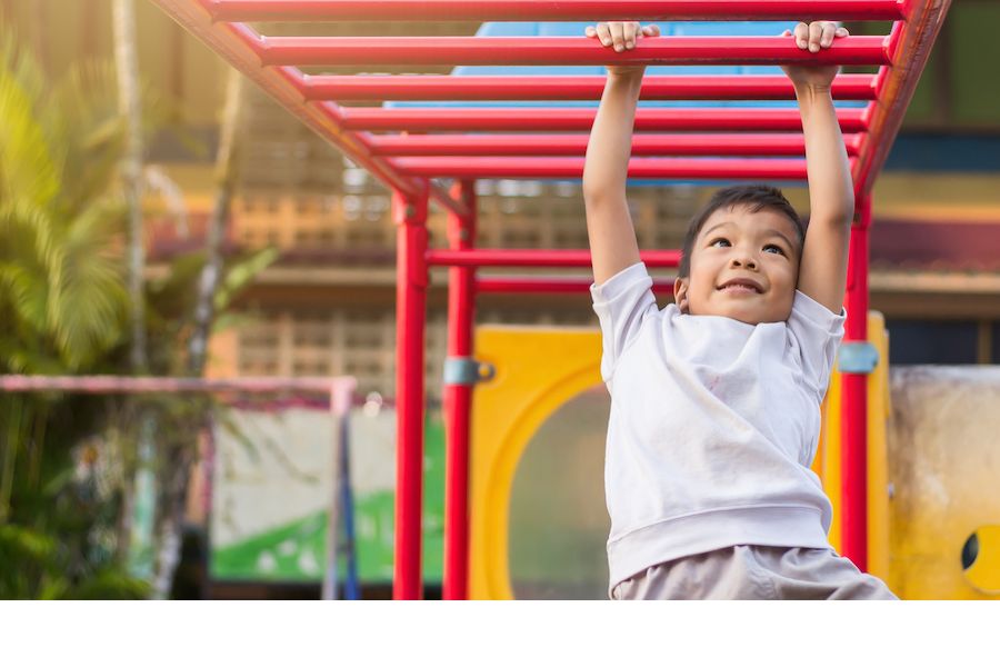 A happy young child hanging from monkey bars
