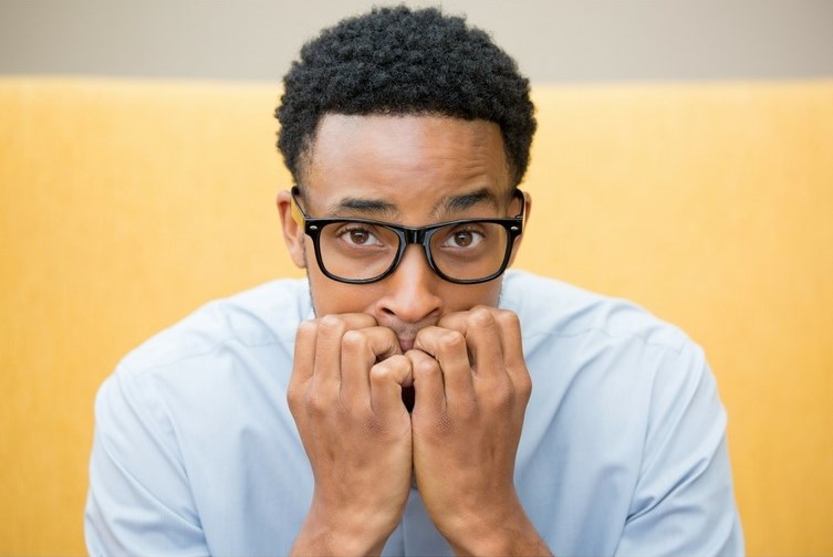 Man sits and stares at camera with a worried expression, and his clenched hands rest against his mouth