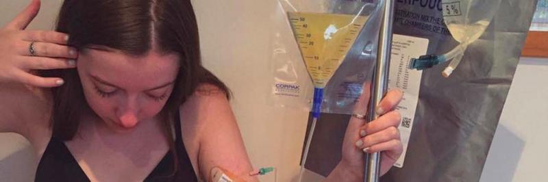 A young woman has an iv in and holds medical equipment while looking down