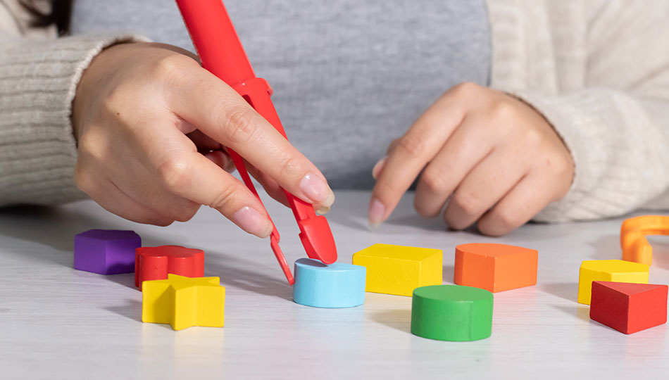 Person's hand using a red pair of tweezers to pick up beads
