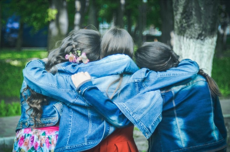 Three girls wearing with their arms over each others shoulders