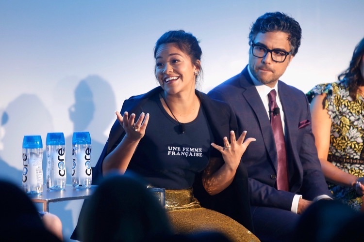 Gina Rodriguez talking at the 2017 Vulture panel, and she sits next to her co-star in a suit