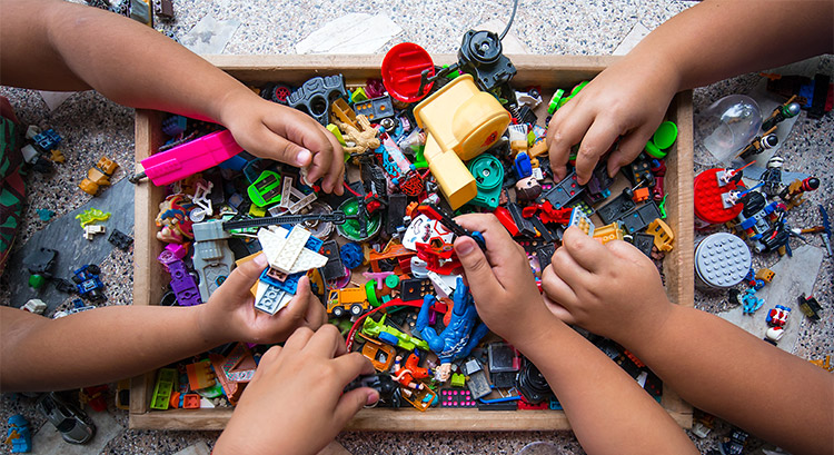 Arms of kids playing with lego in a box.