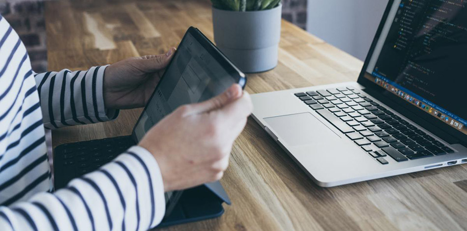 A woman sitting with both an ipad and laptop on the desk in front of her