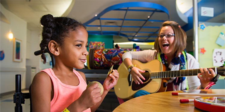 child playing small symbols with teacher playing guitar