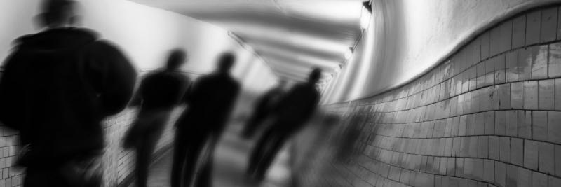 Black and white blurred image of figures walking down a distorted tunnel