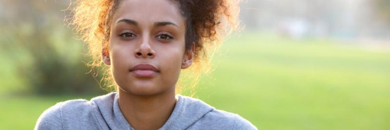 woman in a hoodie sits outside on a sunny day, but she has a somber expression on her face
