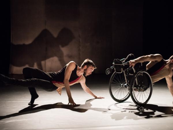 2 men holding a dance position in a horizontal position. One in a wheelchair.