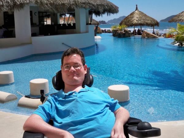 Jon Morrow sits outside smiling in a tropical villa in front of a pool