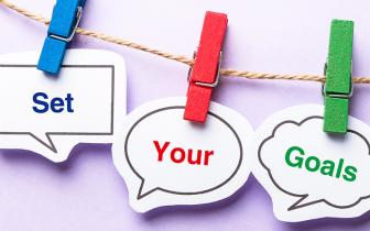 a line with 3 coloured wooden pegs hanging on it. Each peg holds a piece of card with a word on it. The words are set, your and goals